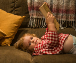 Toddler lying on lounge in nappy holding a book