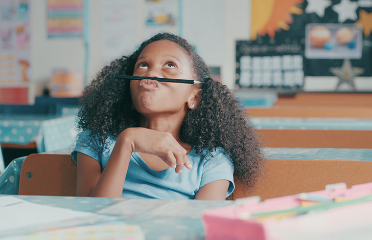 Young black girl at school desk playing with a pencil, not paying attention - feature