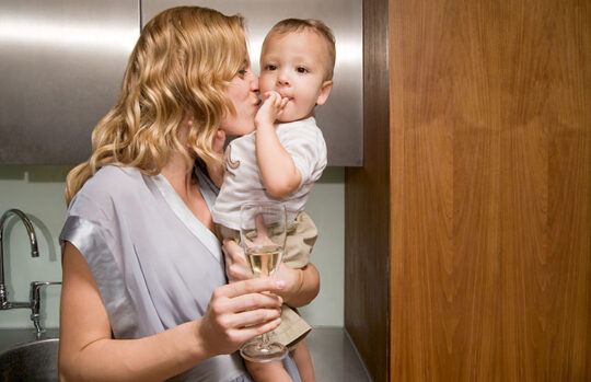 Mother kissing baby while holding a glass of wine - feature