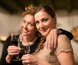 Two smiling women hugging and holding glasses of wine - feature