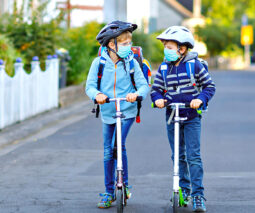 Two kids on scooters in masks