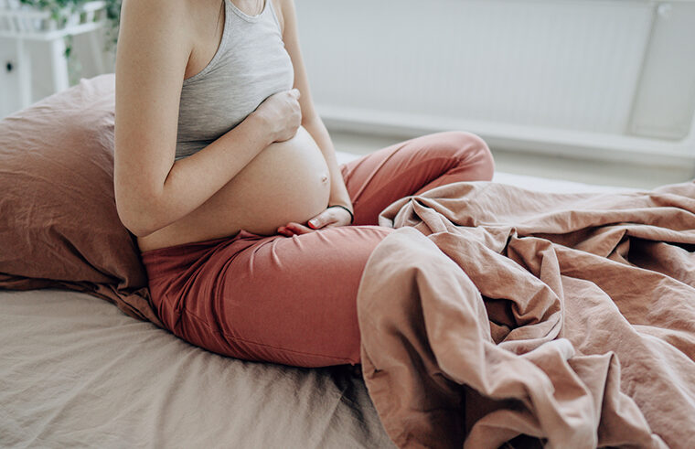 pregnant person holding belly on bed